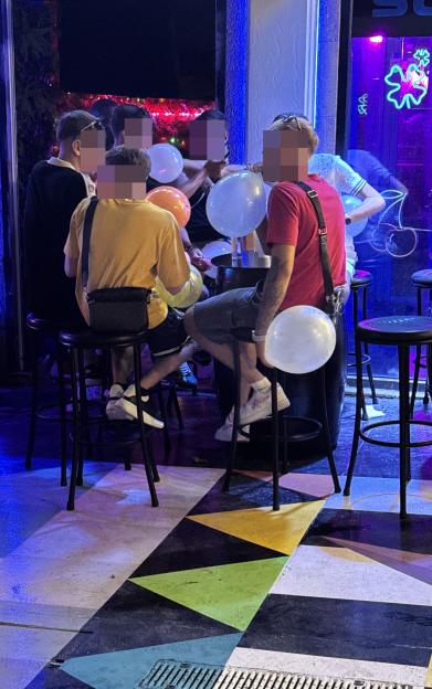 People inhaling nitrous oxide from balloons at a bar.