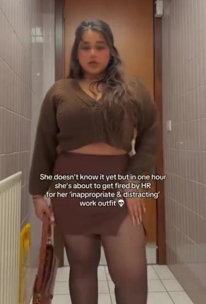Woman in brown sweater and skirt, about to be fired for inappropriate work attire.