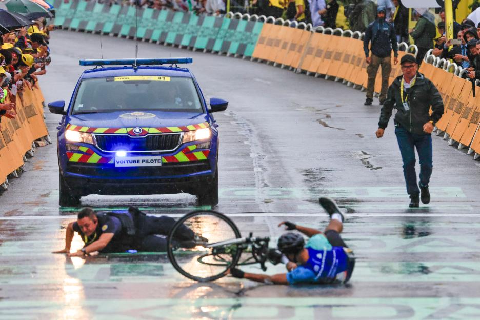 A cyclist crashes on a rain-slicked race course during the Tour de France, stopped by French gendarmes.
