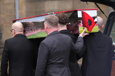 Pallbearers carrying a coffin with a Sheffield United Football Club theme to a funeral service.