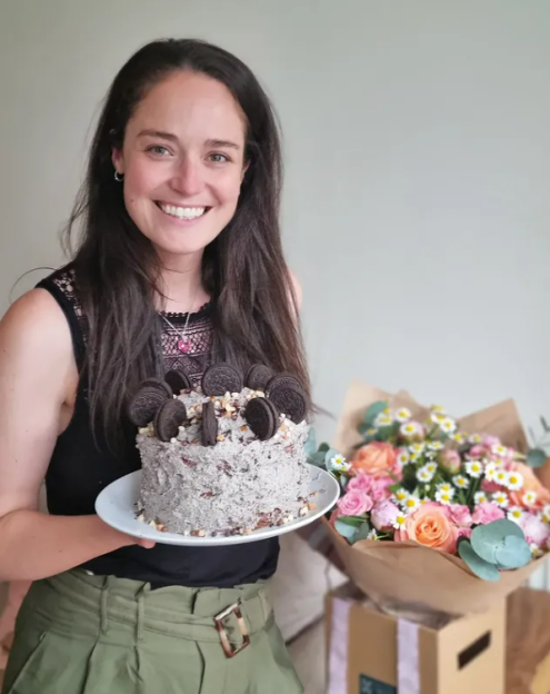 Woman holding a birthday cake and flowers.