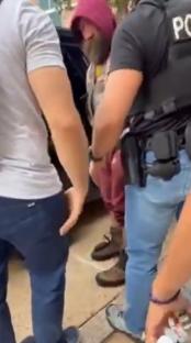 A man in a hooded sweatshirt being detained by police officers.