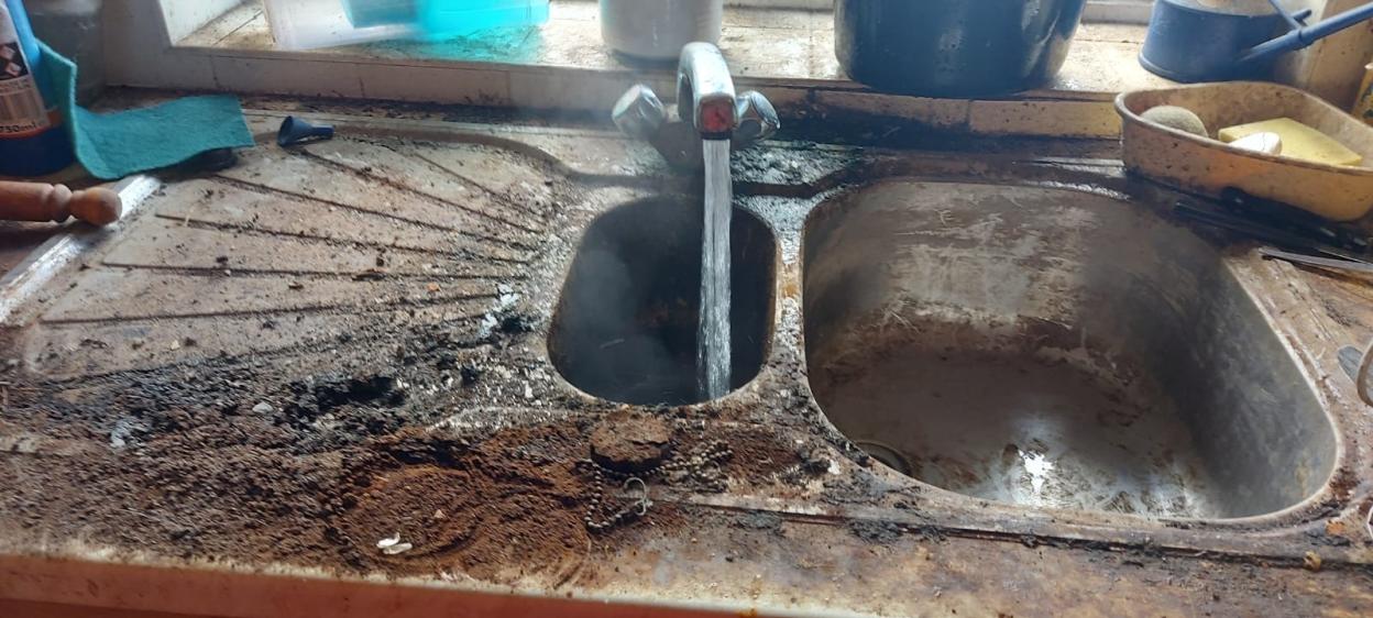 Dirty, rusty double kitchen sink with water running.