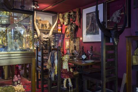 Interior of a museum-like room with a dining table set for two, surrounded by various artifacts and taxidermied animals.