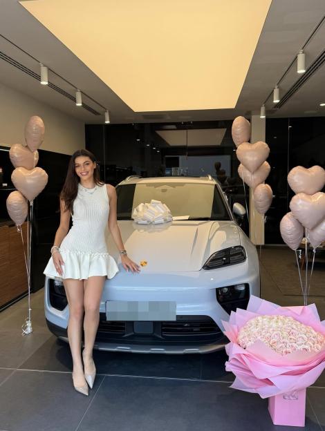 Woman standing in front of a new Porsche with a large bouquet of roses and heart-shaped balloons.