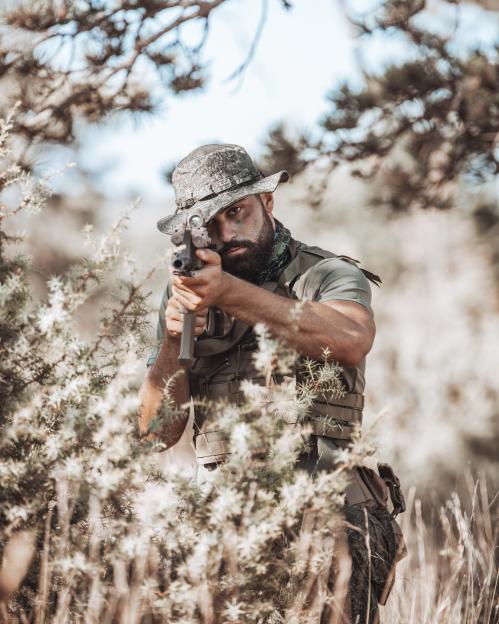 Soldier aiming a rifle while hidden in bushes.