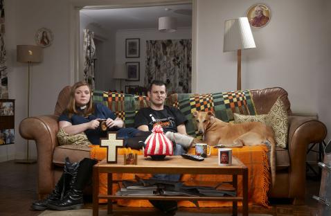 A couple and their dog sit on a couch in their living room.