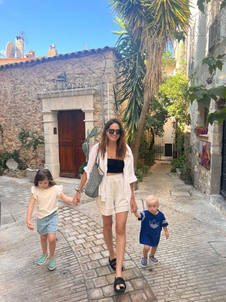 Woman walking down a stone street with two young children holding her hands.