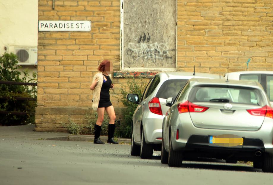 A woman stands on Paradise Street near parked cars.