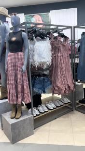 Primark clothing display with red and white plaid dresses, skirts, and tops, denim shorts, and white sandals.