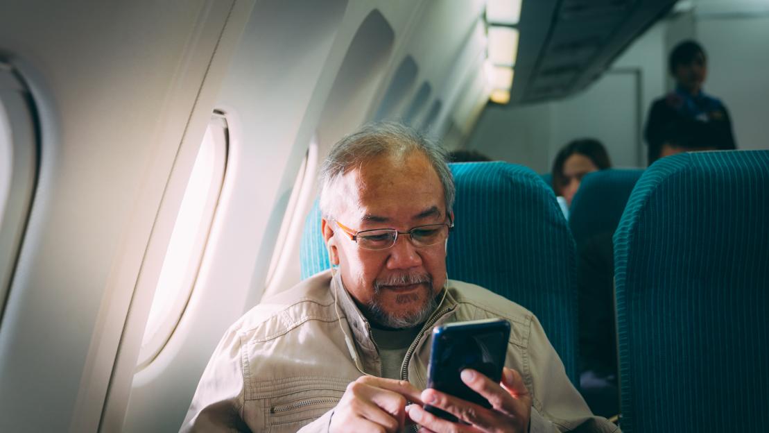 Senior man using smartphone on airplane.