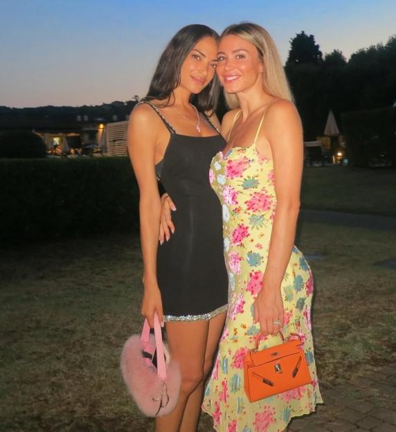 Two women in dresses posing together outdoors.