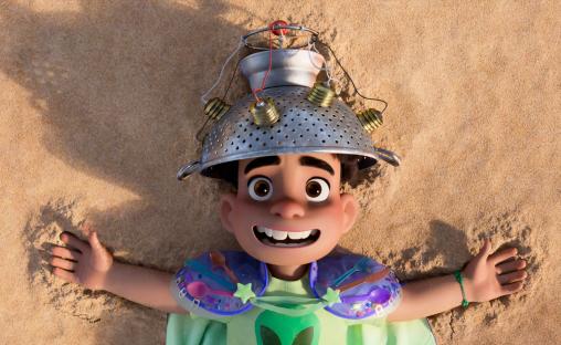 Illustration of Elio, a boy wearing a colander on his head, lying on the sand.