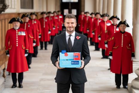 David Beckham holding a Poppy Appeal donation box, with Chelsea Pensioners in the background.