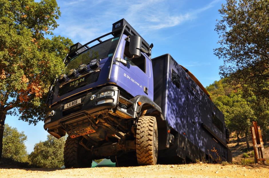 A purple truck camper driving on a dirt road.