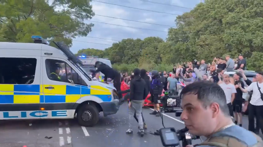 Screenshot of a crowd of people surrounding a police van.