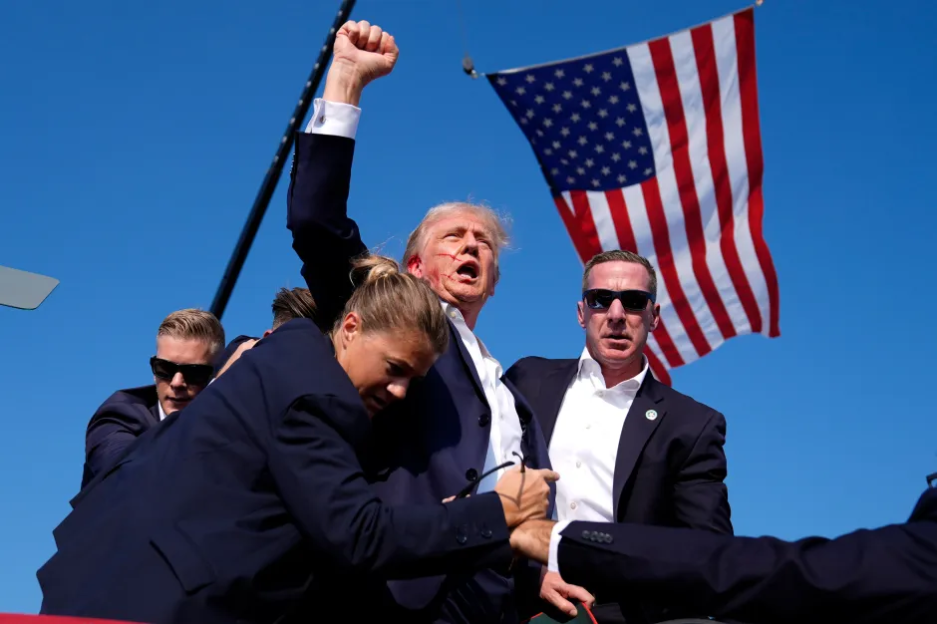 Donald Trump with a bloody face being surrounded by security personnel.