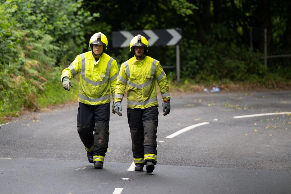 Two firefighters walking on a road.