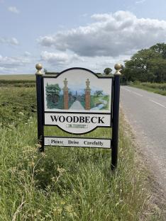 Woodbeck village sign with illustration of gateway and plea to drive carefully.