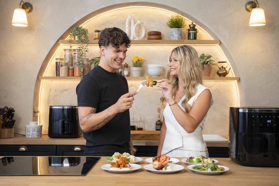 Two people sharing food in a kitchen with an air fryer.