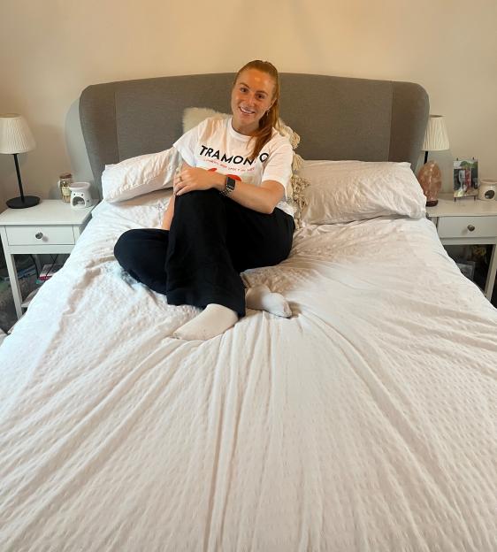 Woman sitting on bed wearing a white t-shirt.