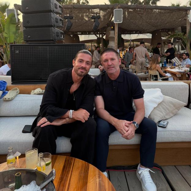 Jack Grealish and another man sitting on a couch outdoors.