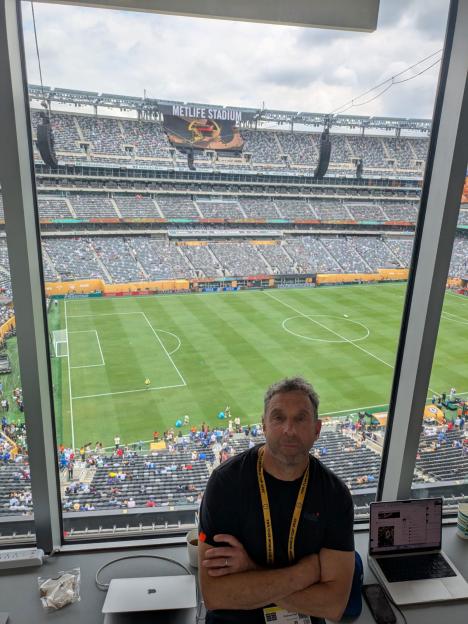 Man sitting in front of a large window overlooking a full soccer stadium.