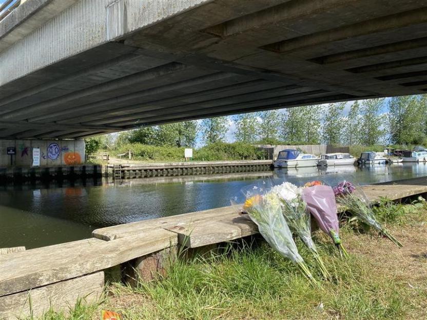 Flowers at a river under a bridge where a teenager died.