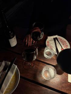 Two glasses of red wine on a table with dinner settings.