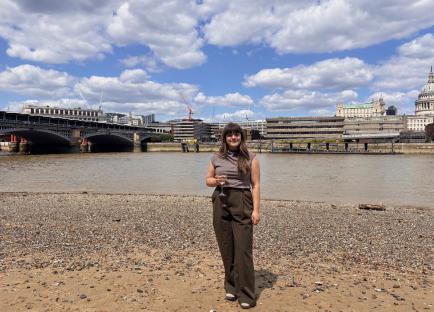 Woman holding a glass of wine on a beach with a city skyline in the background.
