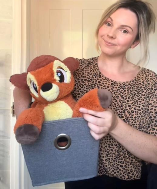 Woman holding a large Bambi plush toy in a gray storage bin.