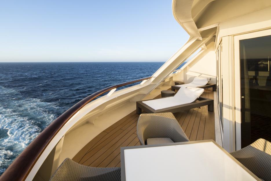 Luxury cruise ship balcony with lounge chairs and table.