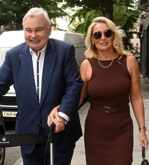 Eamonn Holmes and Katie Alexander walking down a street; Holmes uses a rolling walker.