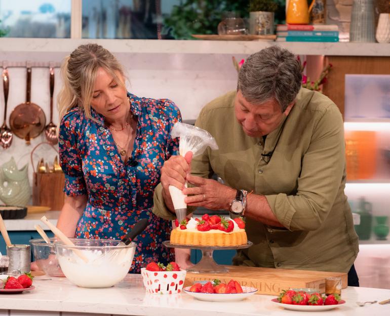 Lisa Faulkner and John Torode decorating a strawberry cake on a TV show.