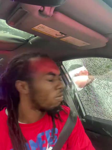 Man in a red shirt in a car with a shattered window.