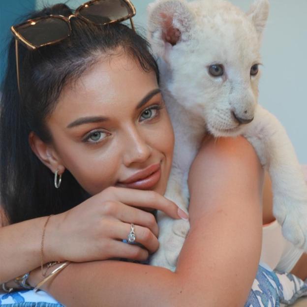 Woman with a white lion cub on her shoulder.