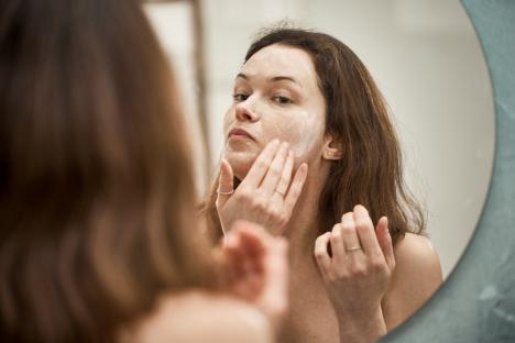Woman applying face cream in a mirror.