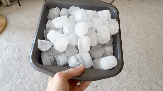 A hand holding a baking pan full of ice cubes.