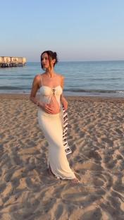 Pregnant woman on a beach holding ultrasound images.