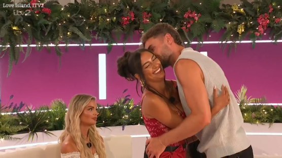 A man embracing a woman while another woman looks on.