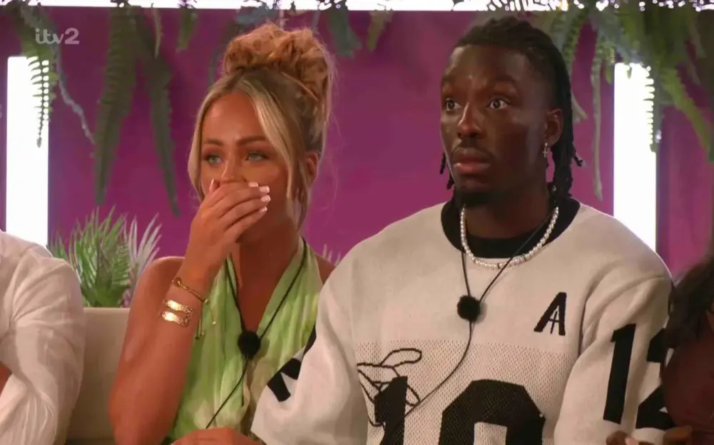 A woman covering her mouth with her hand sits next to a man with a surprised expression.