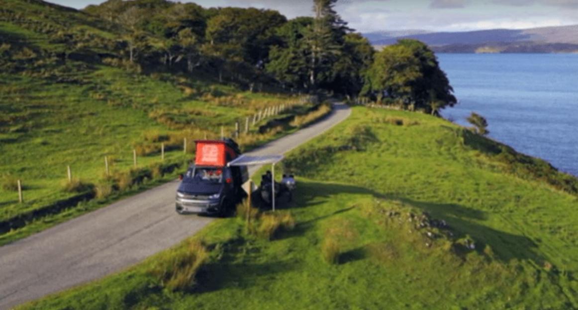 Van parked on a coastal road with people sitting under an awning.