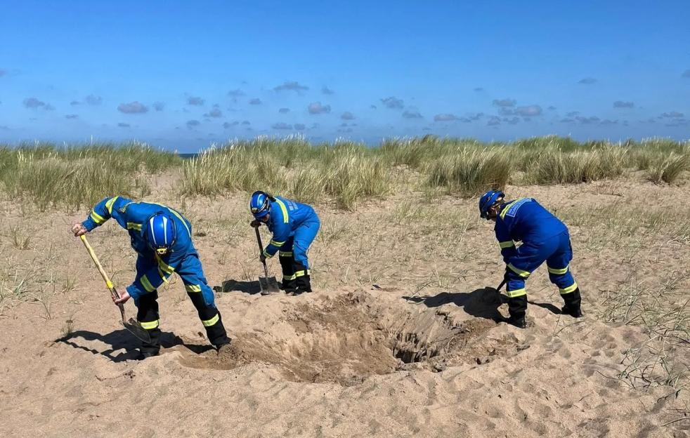 Coastguard members filling a dangerous hole on a beach.