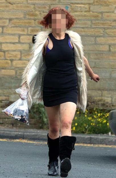 Woman in black dress and fur vest walking down street.