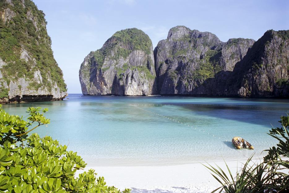 Maya Bay in Thailand, with a boat on a white sand beach and turquoise water surrounded by cliffs.