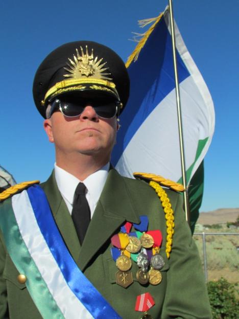 A man in a military uniform stands with a flag.