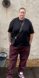 Woman standing outdoors wearing maroon pants and a black shirt.