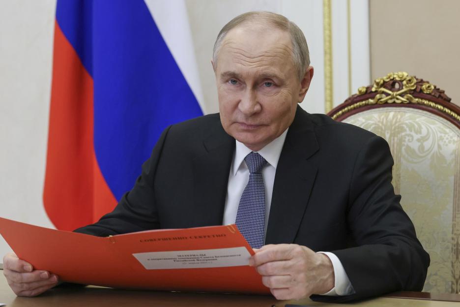 Vladimir Putin reviewing documents at a meeting.