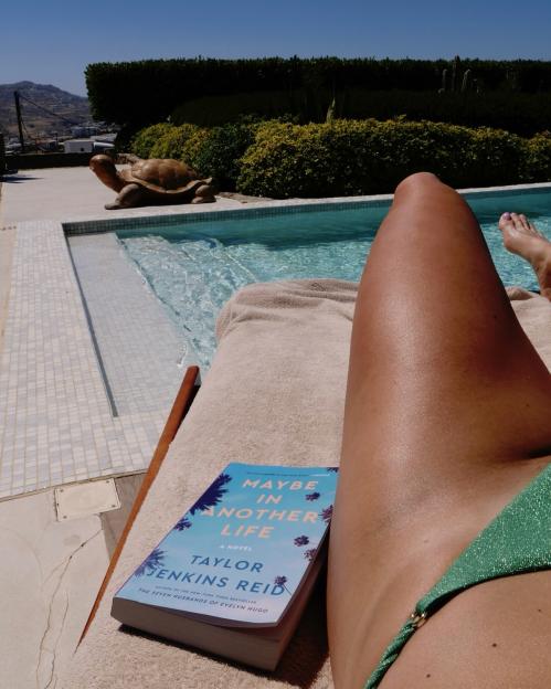 Person's legs by a pool with a book titled