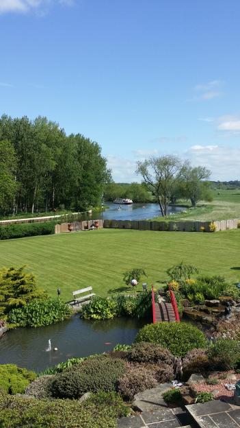 River view from a garden with a pond and red bridge.